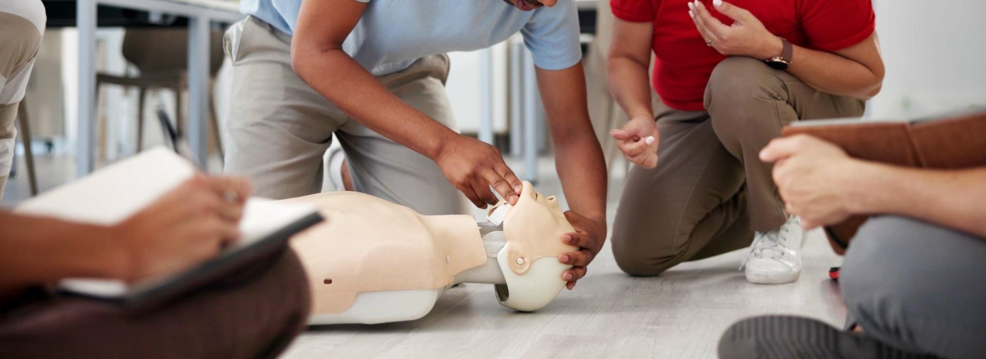 Eine Person übt an einem Reanimationsdummy, während zwei andere Teilnehmer Anweisungen geben und zuschauen.