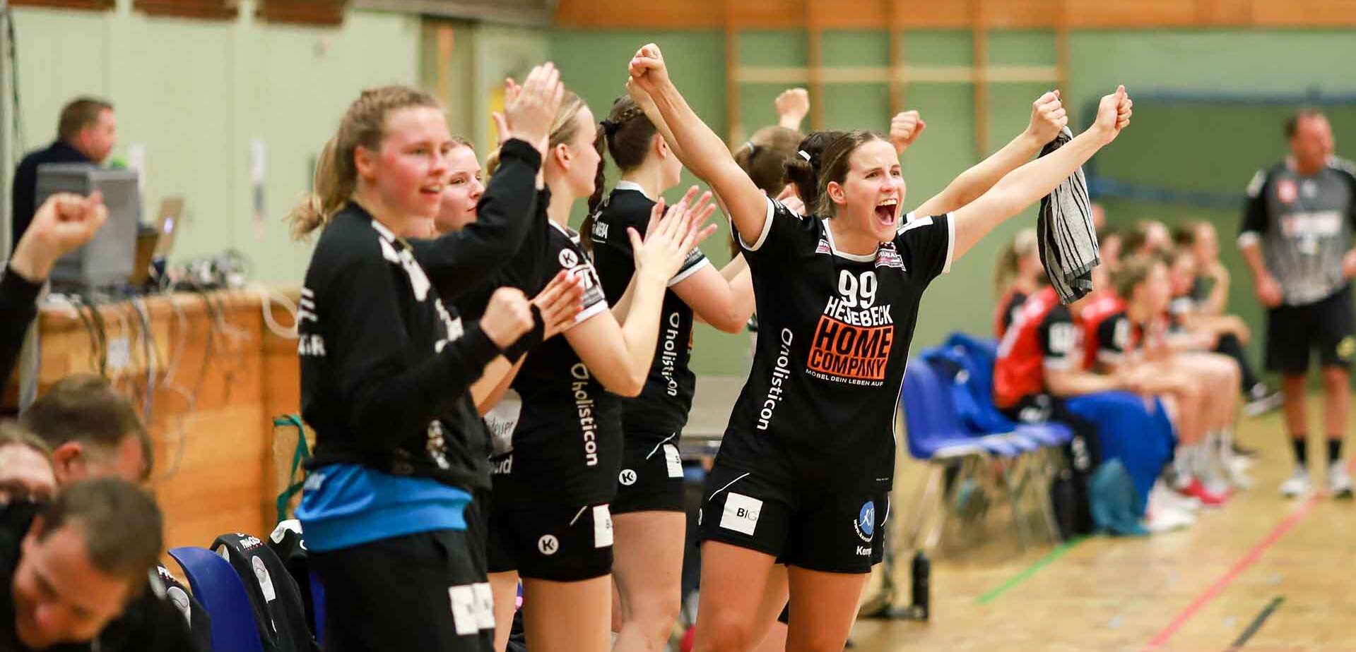 Jubelnde Handballspielerinnen an der Seitenlinie, die ihre Unterstützung für ihr Team zeigen.
