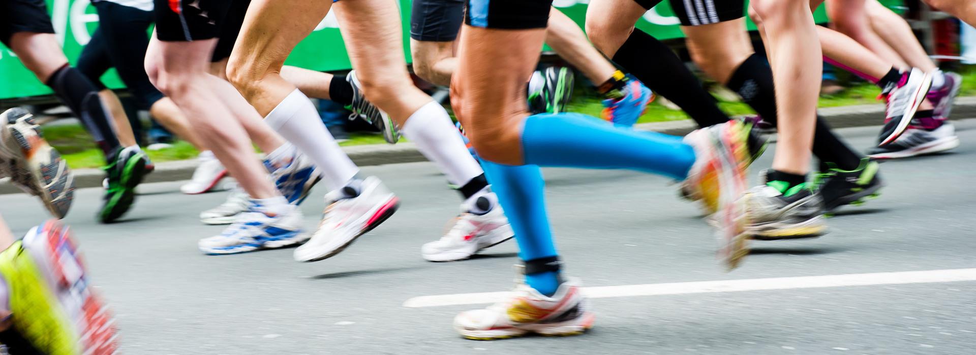 Bunte Laufschuhe rennen in einem Marathon, während Zuschauer im Hintergrund auf der Strecke stehen.